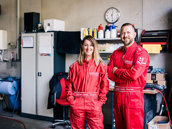 Frau und Mann stehen im roten Rennanzug und blicken in die Kamera.