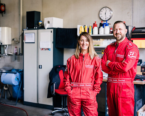 Frau und Mann stehen im roten Rennanzug und blicken in die Kamera.