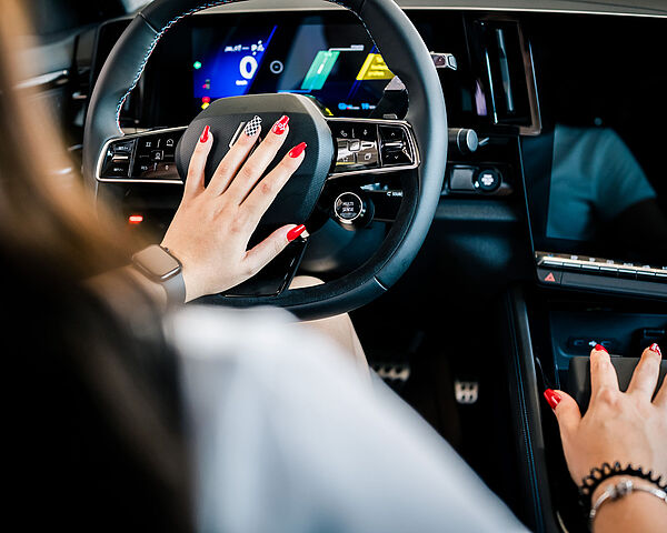 Frau sitzt am Lenkrad in einem Auto. Man sieht ihre lackierten Fingernägel auf denen sich das carplus Logo befindet.