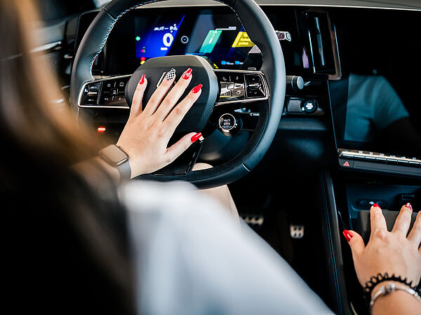 Frau sitzt am Lenkrad in einem Auto. Man sieht ihre lackierten Fingernägel auf denen sich das carplus Logo befindet.