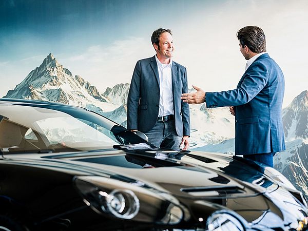 Zwei Männer in Anzügen stehen vor einem neuen Auto.