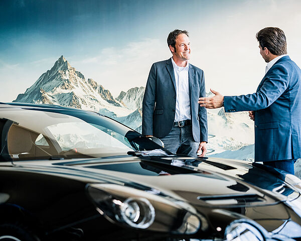 Zwei Männer in Anzügen stehen vor einem neuen Auto. 