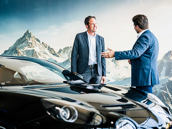 Zwei Männer in Anzügen stehen vor einem neuen Auto. 