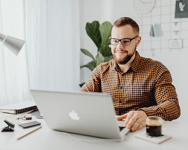 Dunkelhaariger Mann mit Brille sitzt vor dem Laptop.